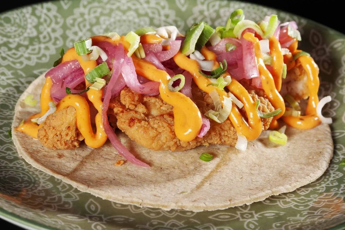 Taco de pollo crispy con salsa naranja y cebolla morada en un plato verde