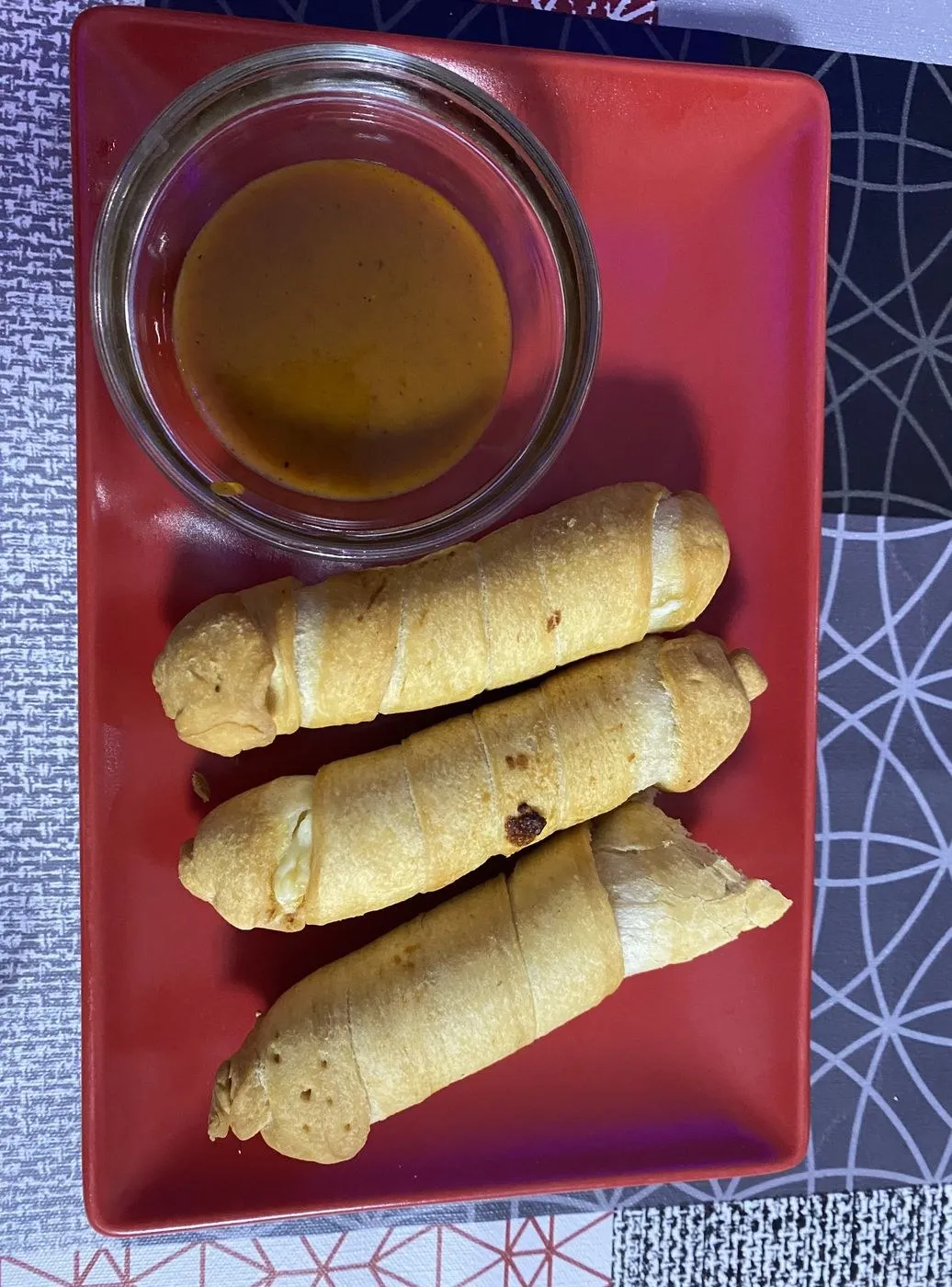 Tres tequeños con un cuenco de salsa sobre una bandeja roja